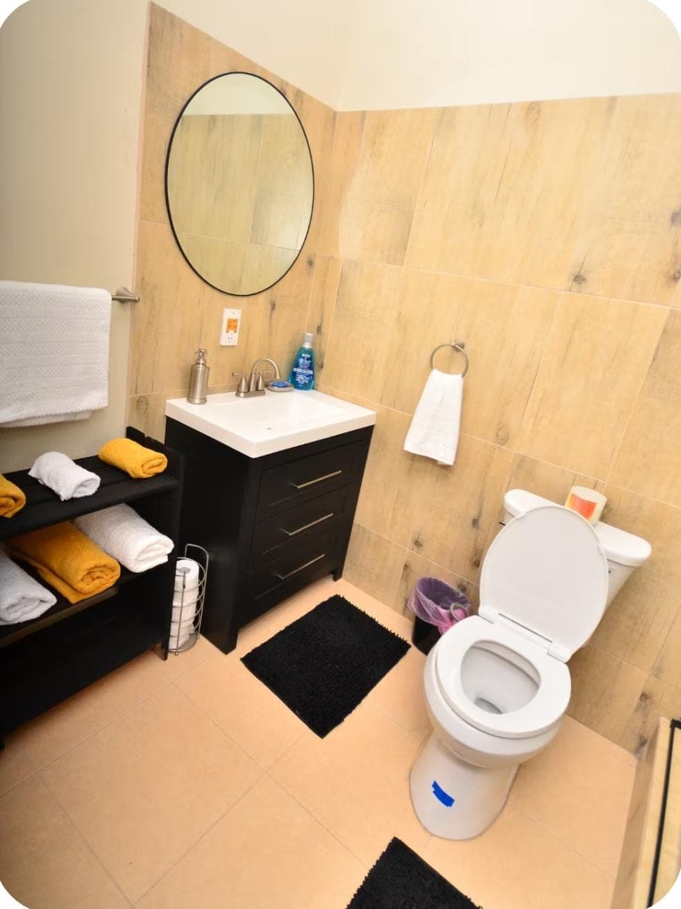 Modern bathroom with dark vanity, oval mirror, and towel storage